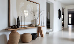 Minimalist entryway with a wooden console table, large framed abstract art, tall candles, and woven vases on the floor.