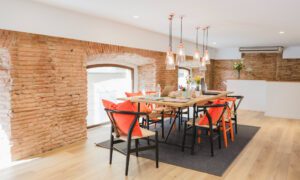 Open-concept meeting area with a wooden table, orange-cushioned chairs, brick walls, and hanging pendant lights.