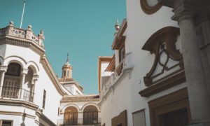 White Mediterranean-style buildings with arches and a copper-domed tower under a clear turquoise sky.