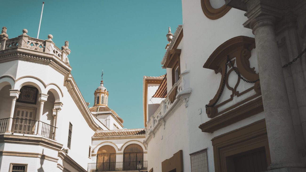 White Mediterranean-style buildings with arches and a copper-domed tower under a clear turquoise sky.