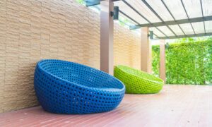 Blue and lime green woven circular lounge chairs on a wooden deck under a glass canopy.